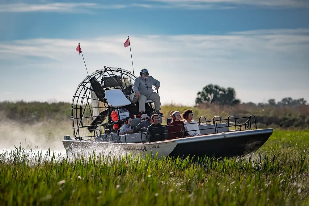 Boggy Creek airboat captain driving guests through tall Florida grass